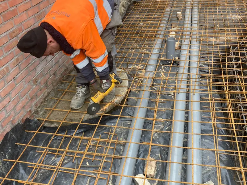vakman in fluo legt wapening en leidingen in vloer