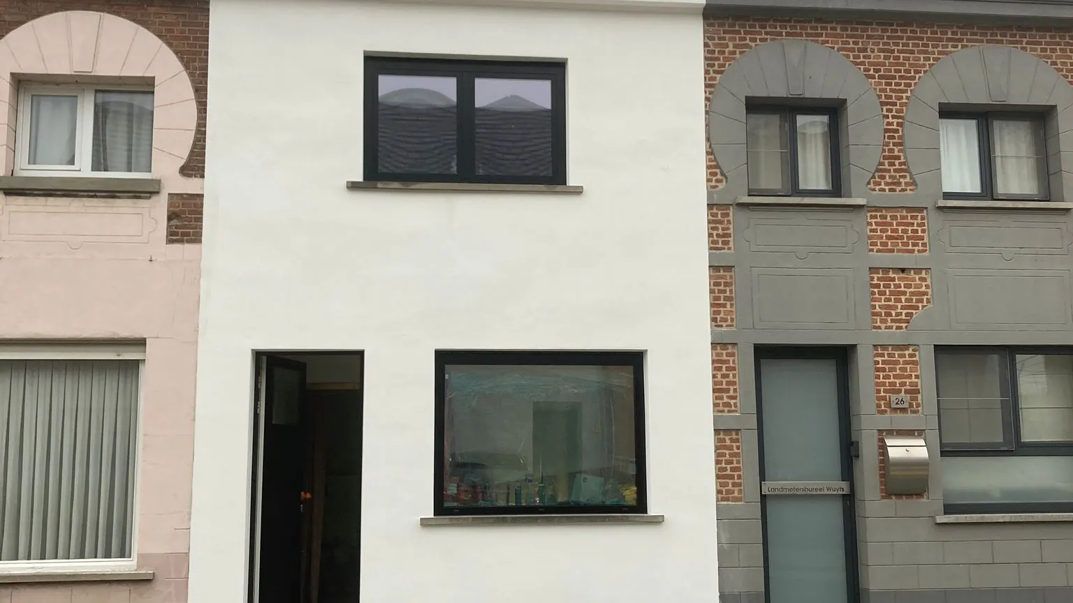 afgewerkte witte voorgevel met nieuw leien dak naast de oude buurwoning, sterk contrast