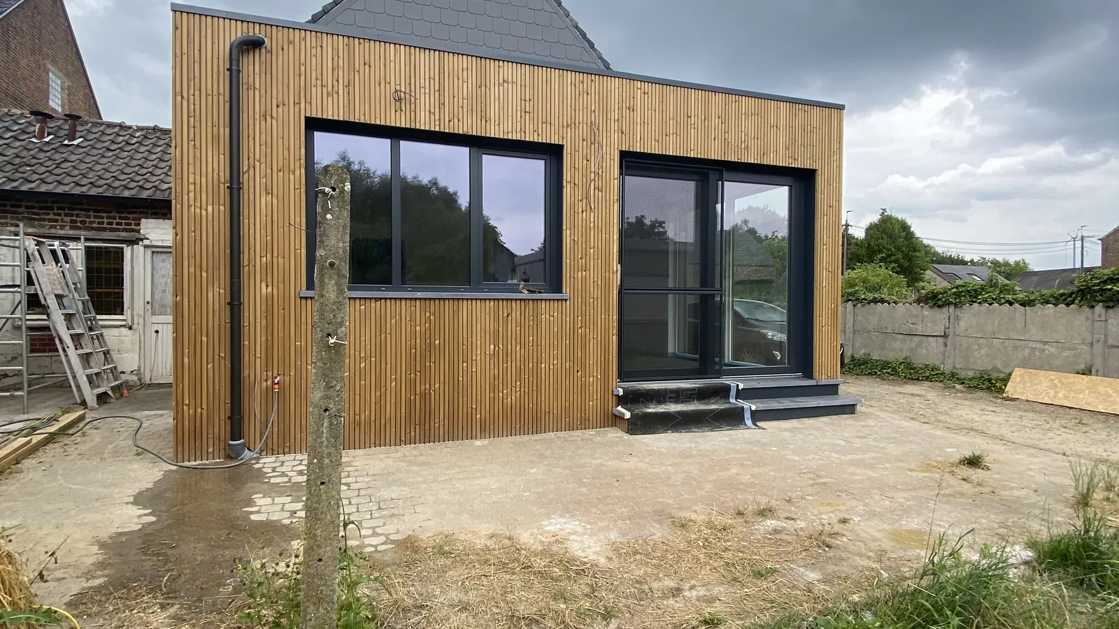 afgewerkte uitbouw met houten gevelbekleding en grote ramen onder dramatische lucht