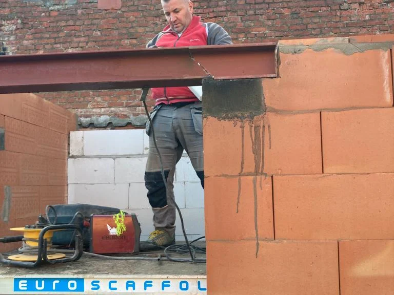 vakman op muur bij stalen ligger, blauwe lucht