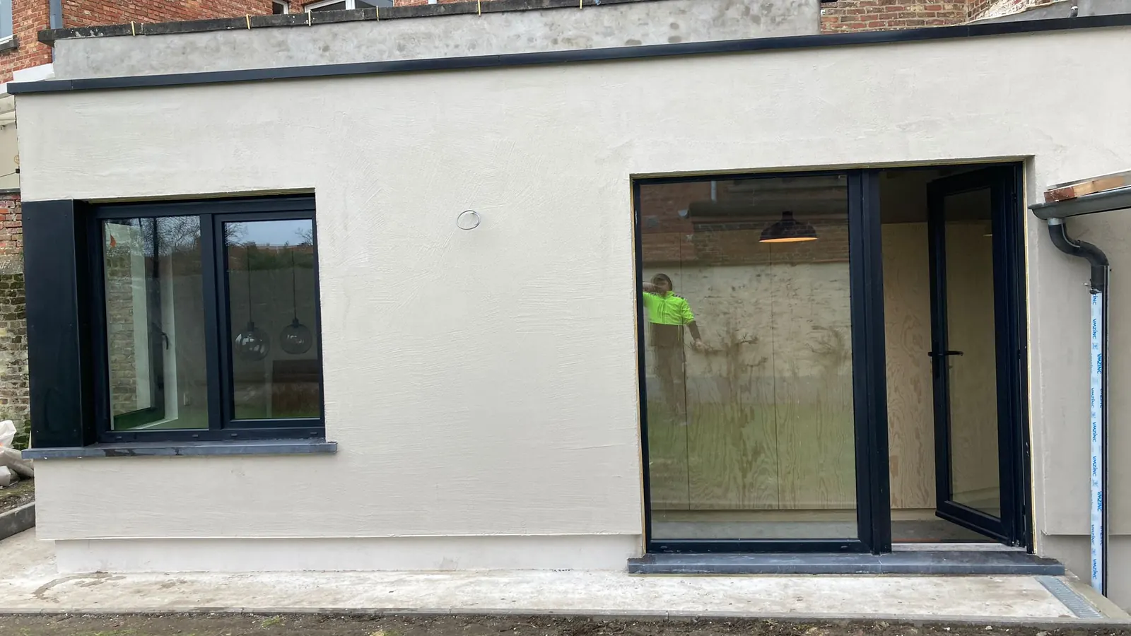 afgewerkte witte achterbouw met grote zwarte ramen en gras, strak
