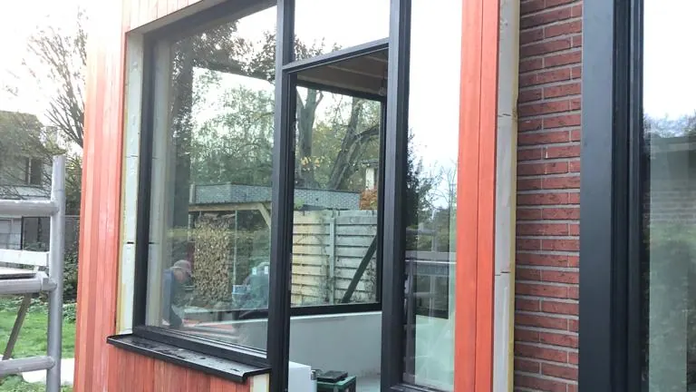 uitbouw met rode houten gevelbekleding en zwarte ramen, strak en modern