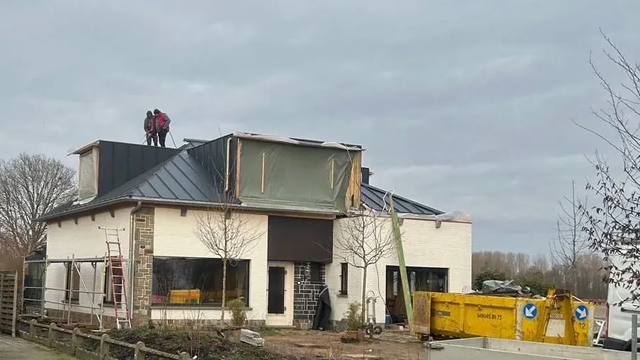 woning met nieuw antraciet dak en dakkapel in avondlicht, werf op de achtergrond