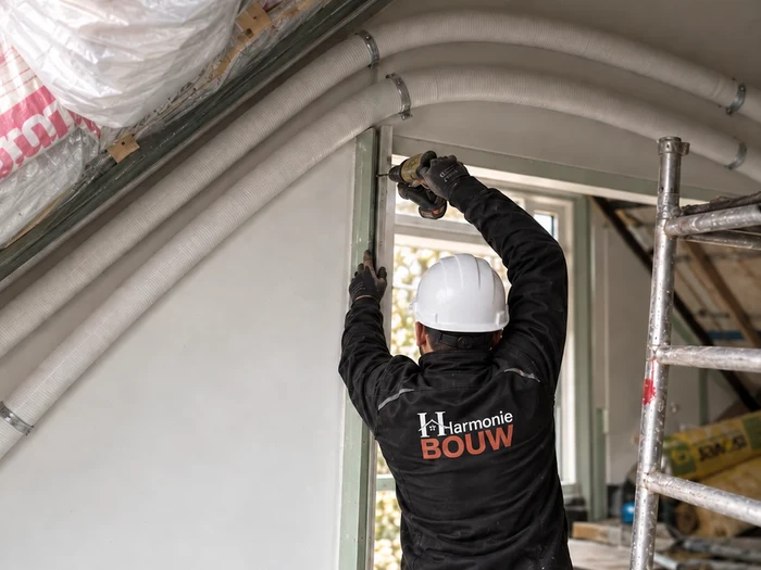 Vakman van Harmonie Bouw met helm en bedrijfskledij stelt een raamkader in de zolder
